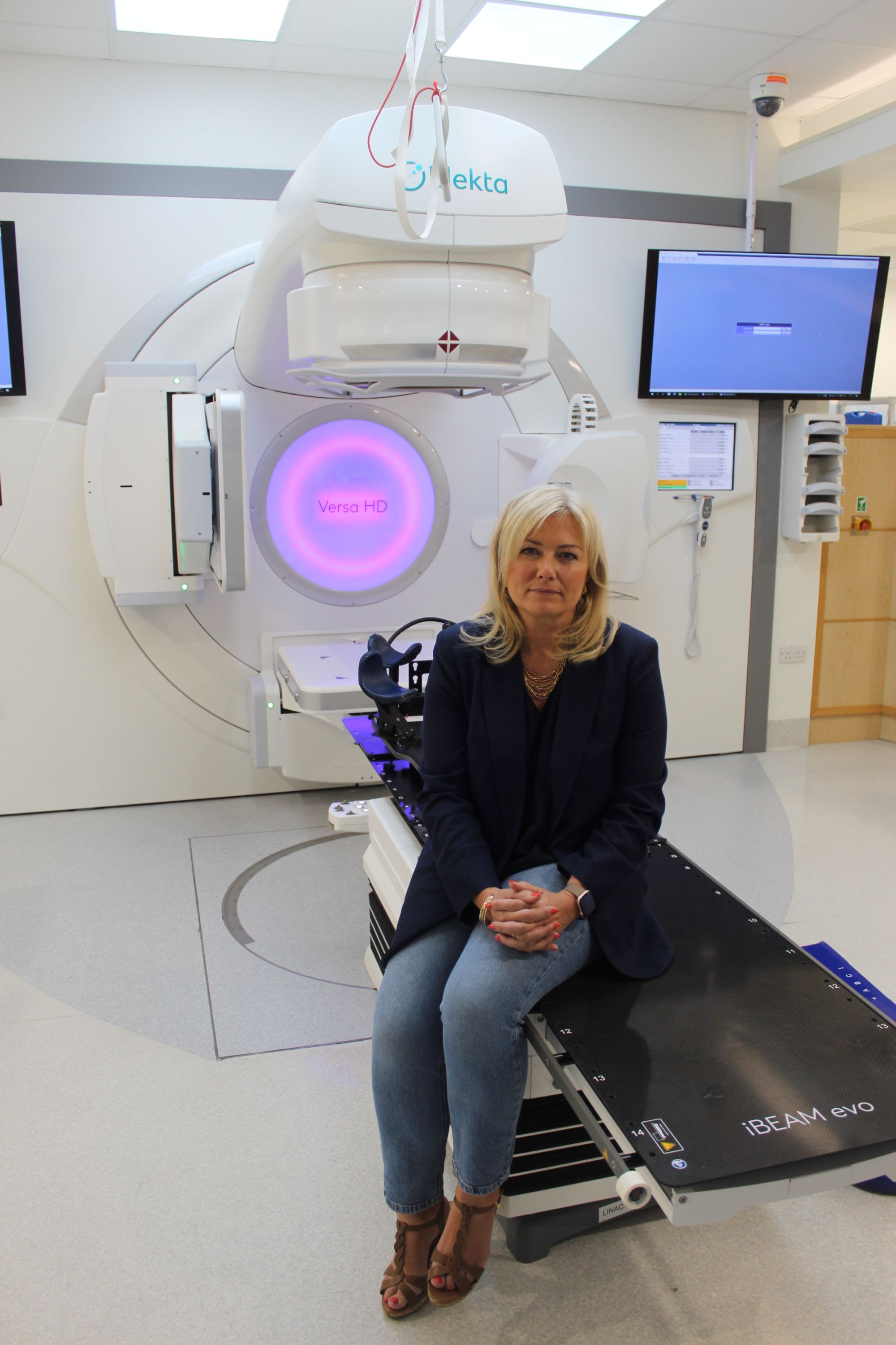 Leanne sitting in front of a linac laser machine where SGRT has been installed