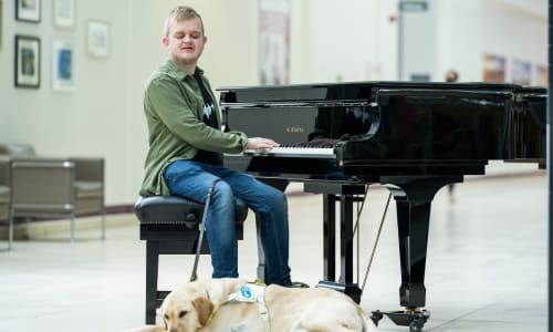 Louis playing the piano in the Bexley Wing with his guide dog Kizzy