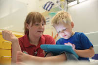 Leukaemia patient Leo playing on a tablet with play Leader Katie