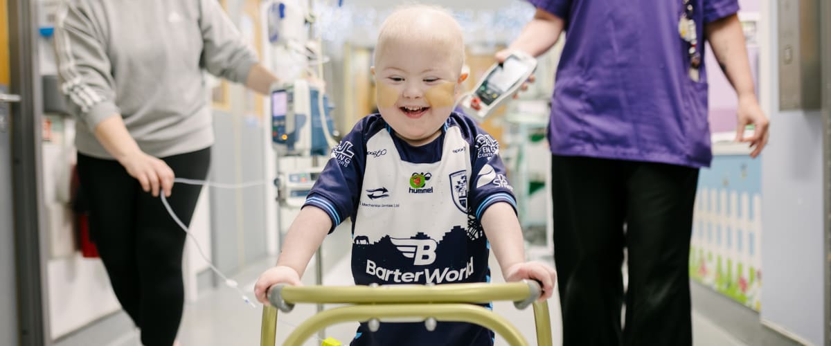 Reggie smiling while using a walker on a corridor of award at Leeds Childrens Hospital