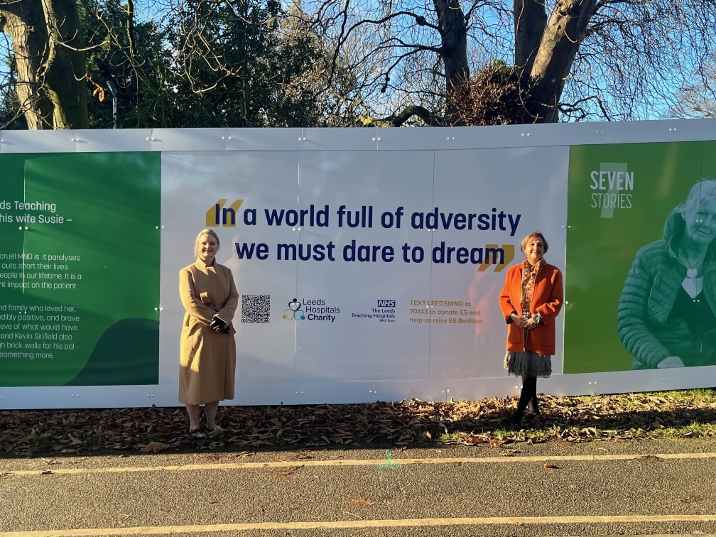 Esther Wakeman and Dr Agam Jung stand in front of the hoardings with a quote from Rob that reads 